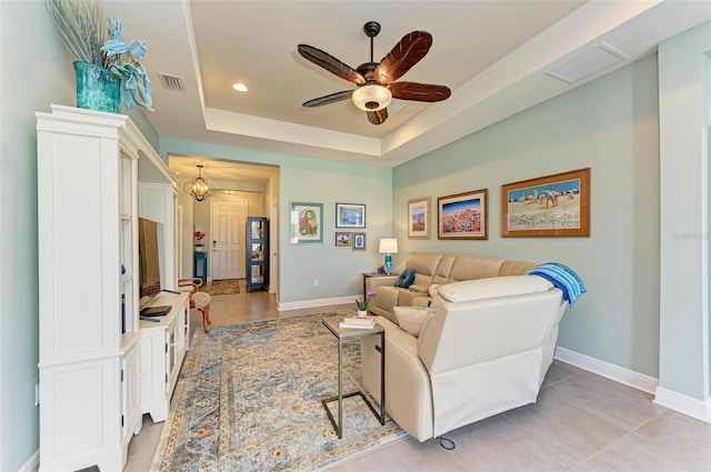 living room with a raised ceiling, light tile patterned floors, and ceiling fan with notable chandelier