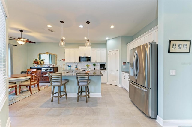 kitchen with white cabinets, stainless steel appliances, a kitchen island with sink, and dark stone counters