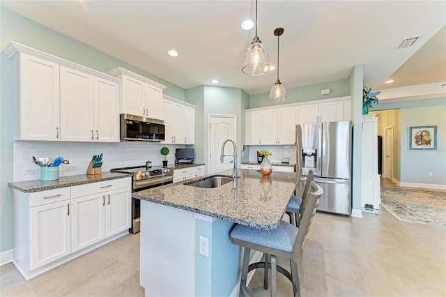 kitchen with a center island with sink, sink, dark stone countertops, appliances with stainless steel finishes, and white cabinetry