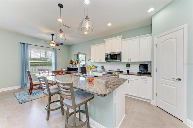 kitchen with white cabinetry, stainless steel appliances, a kitchen island with sink, and dark stone counters