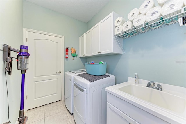 clothes washing area featuring sink, cabinets, washing machine and dryer, a textured ceiling, and light tile patterned floors