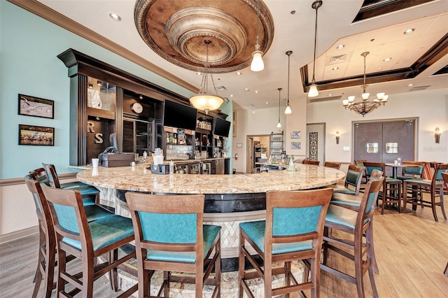 bar featuring ornamental molding, a tray ceiling, hanging light fixtures, and light wood-type flooring