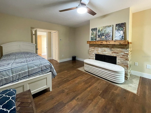 bedroom with a textured ceiling, a stone fireplace, dark hardwood / wood-style floors, and ceiling fan