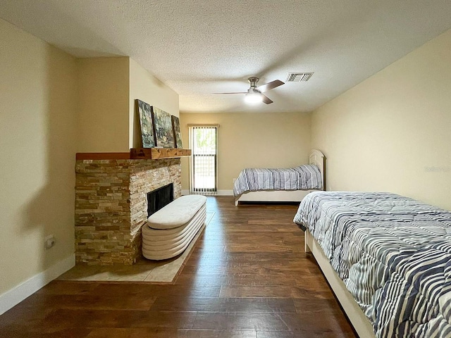 bedroom featuring a textured ceiling, a stone fireplace, ceiling fan, and dark wood-type flooring