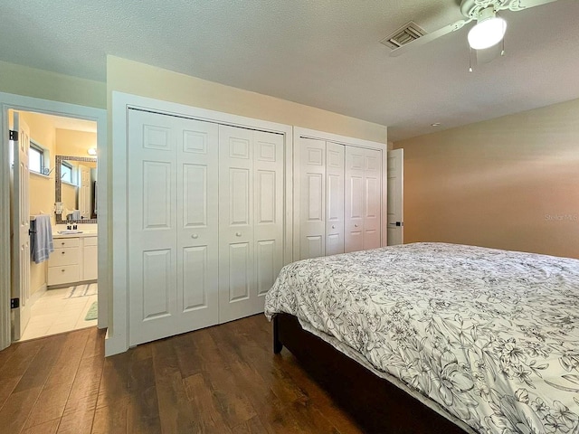 bedroom featuring two closets, ceiling fan, sink, and dark hardwood / wood-style flooring