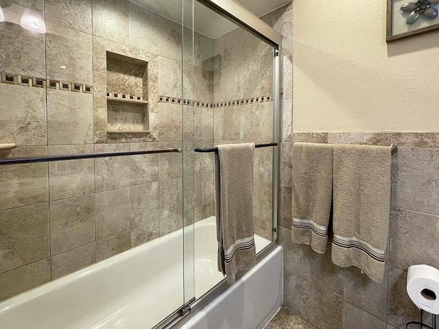 bathroom featuring tile walls and combined bath / shower with glass door