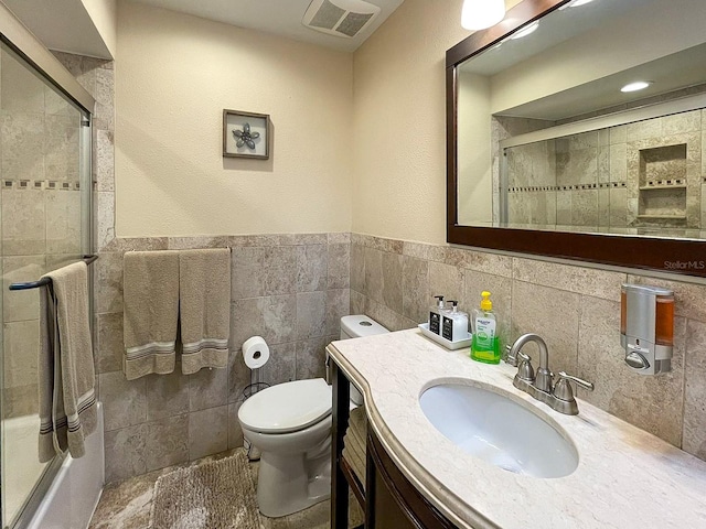 bathroom with tile walls, a shower with door, vanity, and toilet