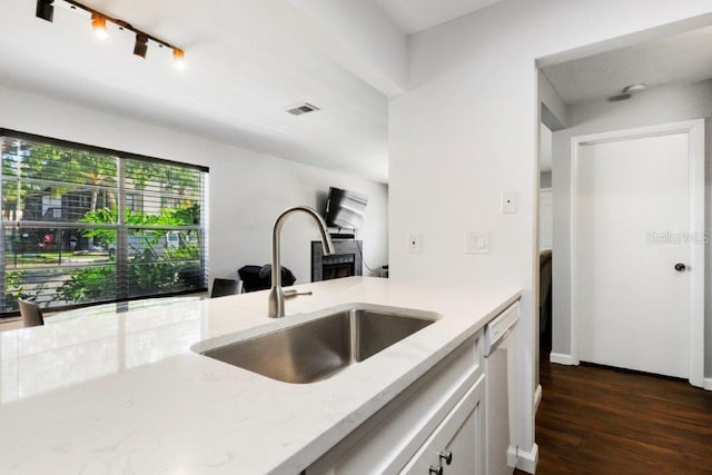 kitchen with white cabinetry, dark wood-type flooring, light stone countertops, dishwasher, and sink