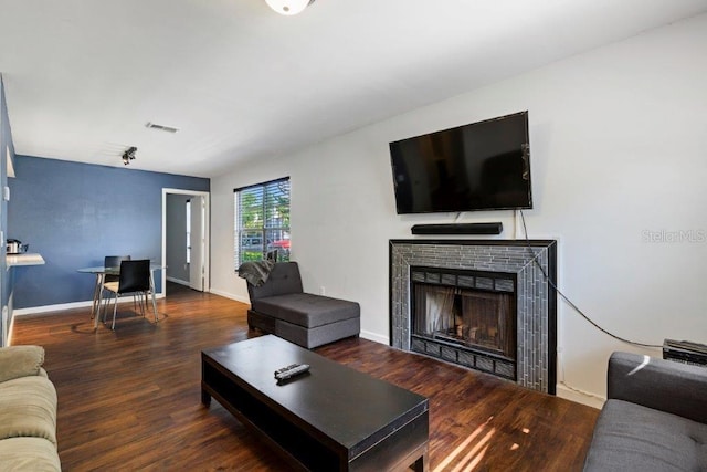 living room with a tile fireplace and dark wood-type flooring