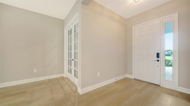 entrance foyer featuring lofted ceiling, light hardwood / wood-style floors, and a textured ceiling