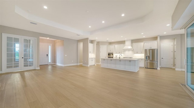 unfurnished living room with sink, a raised ceiling, and light hardwood / wood-style flooring