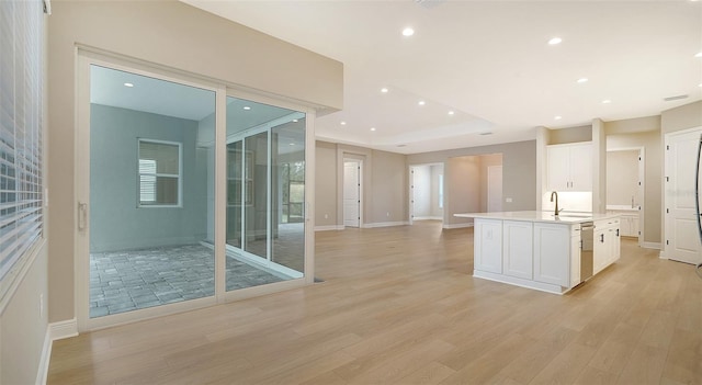 kitchen with light hardwood / wood-style floors, white cabinets, a center island with sink, and sink