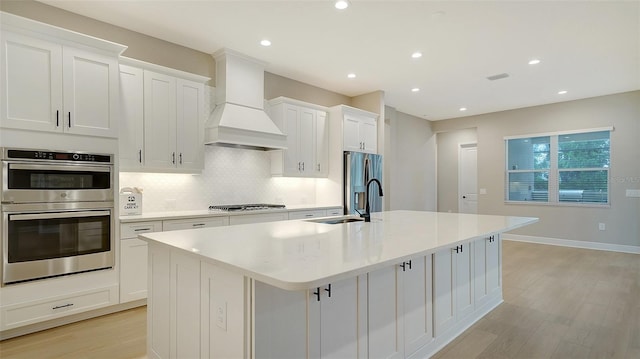 kitchen with custom exhaust hood, white cabinets, a kitchen island with sink, and stainless steel appliances