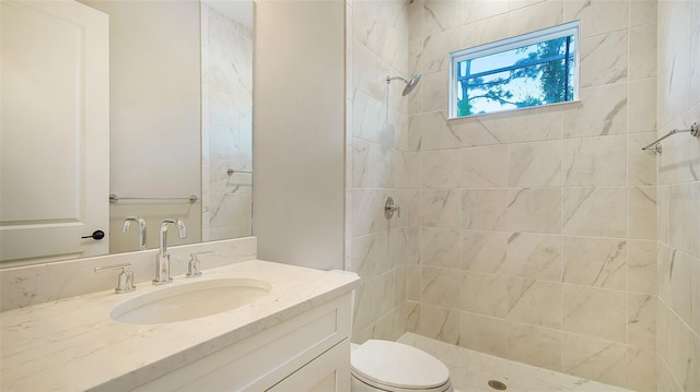 bathroom with a tile shower, vanity, and toilet