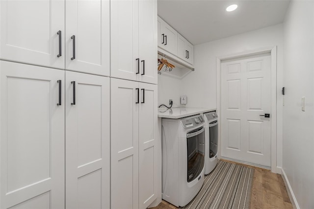 clothes washing area with cabinets, light hardwood / wood-style floors, and washer and dryer