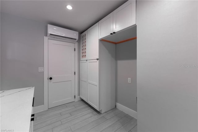 kitchen featuring light stone countertops, white cabinets, light hardwood / wood-style floors, and a wall mounted AC