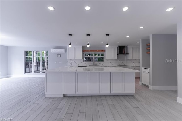 kitchen featuring pendant lighting, light wood-type flooring, a wall unit AC, and wall chimney range hood