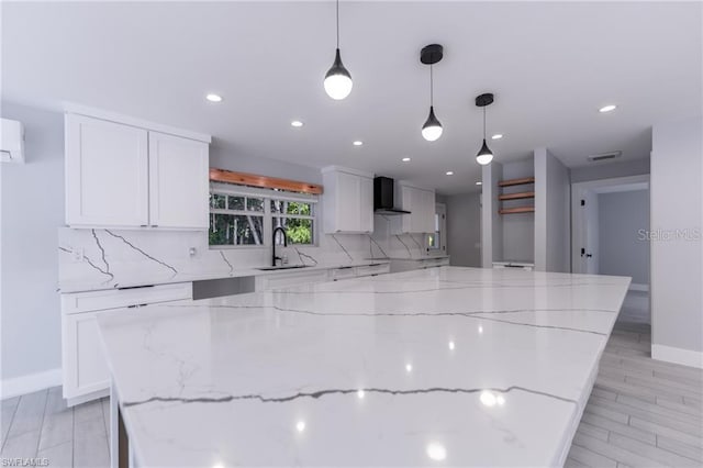 kitchen with wall chimney exhaust hood, white cabinets, light stone counters, and decorative light fixtures