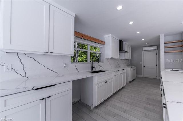 kitchen with white cabinets, sink, wall chimney exhaust hood, light stone countertops, and decorative backsplash