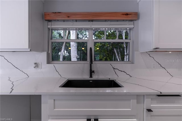 kitchen with backsplash, white cabinets, light stone counters, and sink