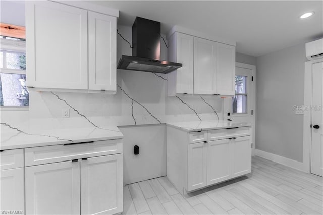 kitchen featuring wall chimney exhaust hood, tasteful backsplash, light stone counters, and white cabinets