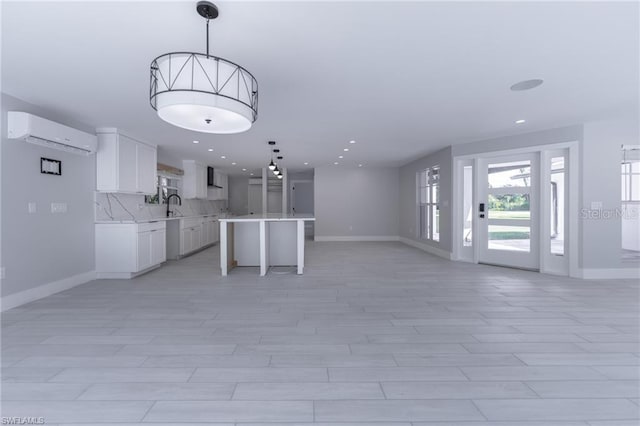 interior space featuring hanging light fixtures, white cabinets, a center island, a wall unit AC, and sink