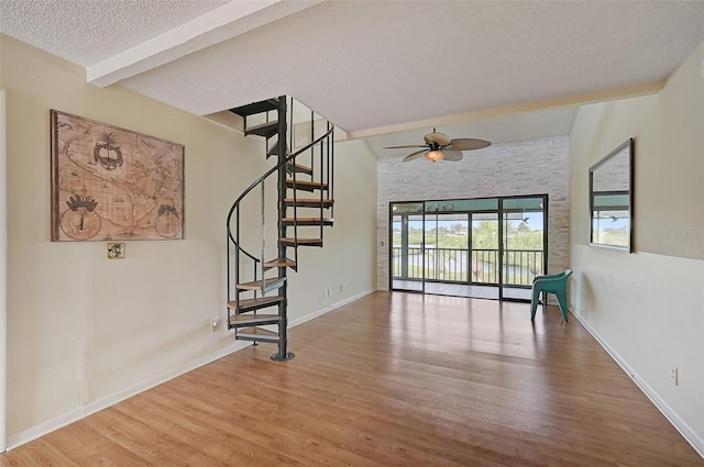 interior space with beam ceiling, a textured ceiling, wood finished floors, baseboards, and stairs