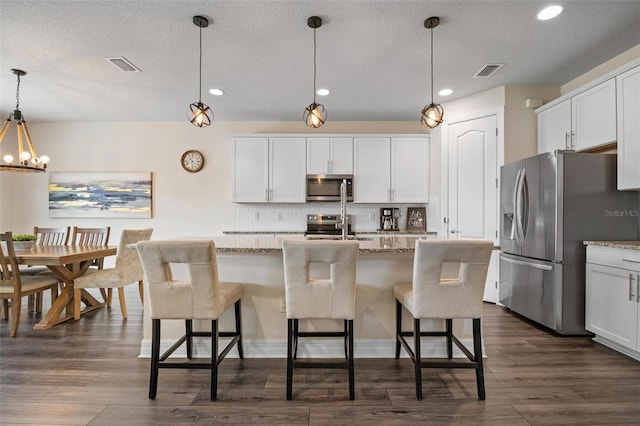 kitchen featuring appliances with stainless steel finishes, a center island with sink, light stone countertops, and decorative light fixtures