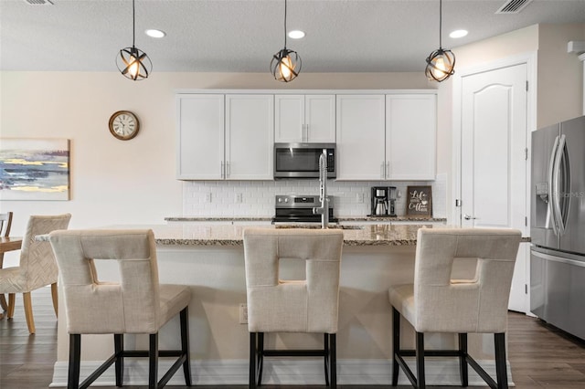 kitchen featuring stainless steel appliances, decorative light fixtures, and a kitchen island with sink