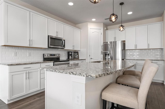 kitchen featuring an island with sink, white cabinets, light stone countertops, dark hardwood / wood-style flooring, and stainless steel appliances