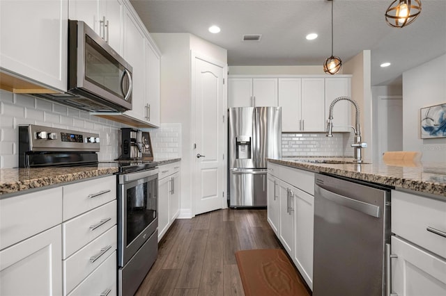 kitchen with appliances with stainless steel finishes, light stone counters, white cabinets, dark hardwood / wood-style flooring, and decorative light fixtures