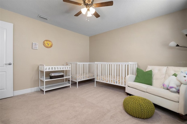 bedroom with ceiling fan, a crib, and carpet flooring