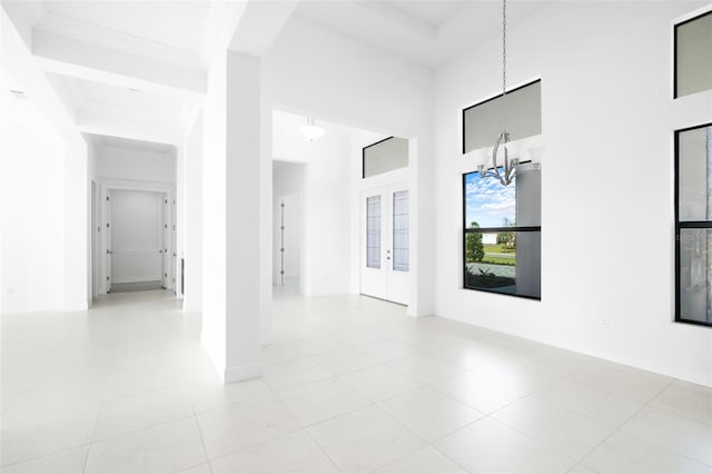 empty room featuring a high ceiling, light tile patterned floors, french doors, and a notable chandelier