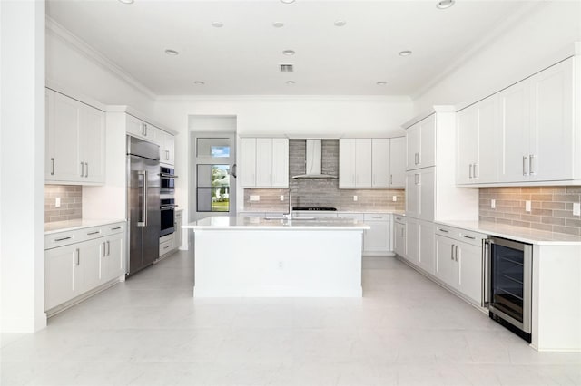 kitchen with white cabinets, wine cooler, a kitchen island with sink, wall chimney range hood, and stainless steel appliances