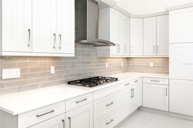 kitchen with white cabinets, stainless steel gas cooktop, wall chimney exhaust hood, backsplash, and light stone countertops