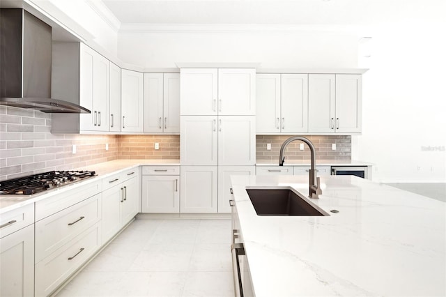 kitchen featuring light stone counters, sink, stainless steel gas stovetop, white cabinets, and wall chimney range hood