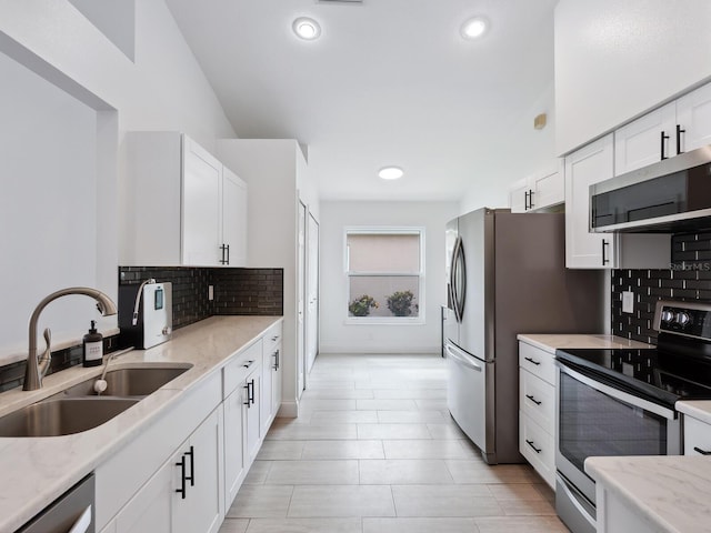 kitchen with appliances with stainless steel finishes, white cabinetry, light stone counters, backsplash, and sink