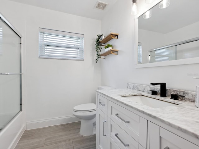 full bathroom featuring hardwood / wood-style floors, combined bath / shower with glass door, vanity, and toilet