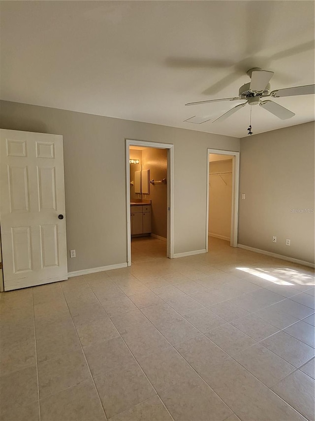 unfurnished bedroom featuring ceiling fan, ensuite bathroom, light tile patterned floors, and a spacious closet