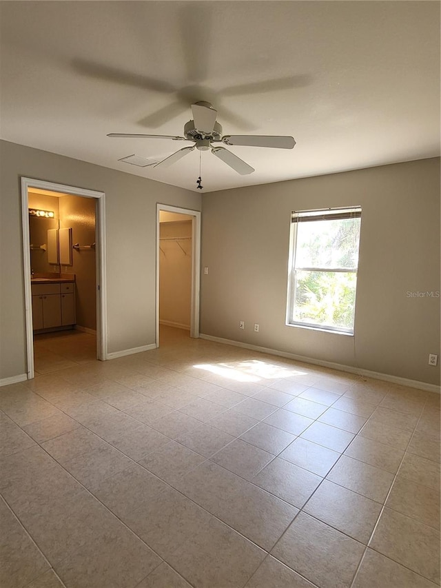 unfurnished bedroom with ceiling fan, ensuite bathroom, a walk in closet, a closet, and light tile patterned floors