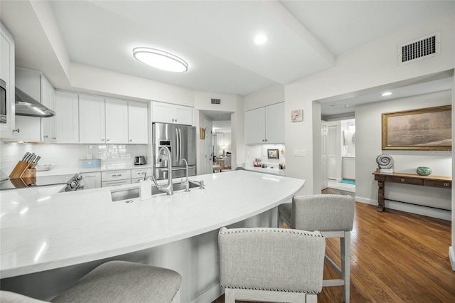 kitchen featuring backsplash, dark hardwood / wood-style floors, stainless steel refrigerator with ice dispenser, white cabinets, and kitchen peninsula