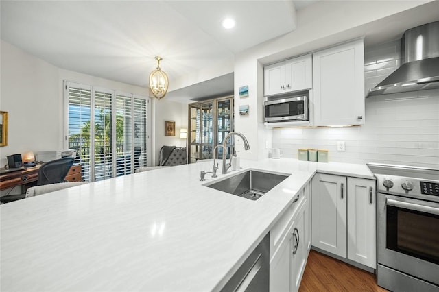 kitchen with appliances with stainless steel finishes, decorative light fixtures, sink, white cabinets, and wall chimney range hood