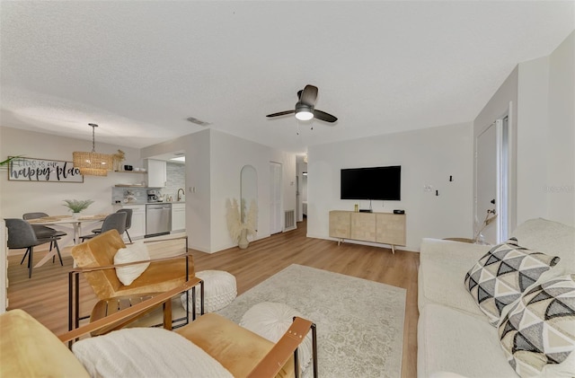 living room with ceiling fan, a textured ceiling, sink, and light hardwood / wood-style floors