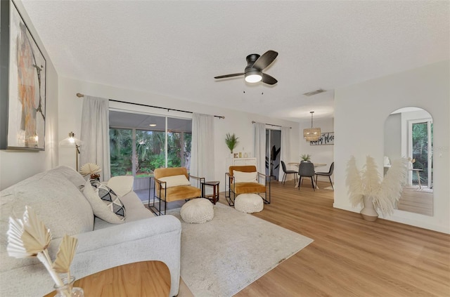 living room featuring light wood-type flooring, a healthy amount of sunlight, a textured ceiling, and ceiling fan