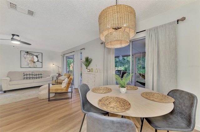 dining area featuring ceiling fan with notable chandelier, a textured ceiling, and light wood-type flooring