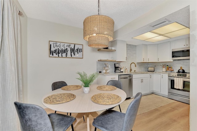 dining space featuring an inviting chandelier, light wood-type flooring, a textured ceiling, and sink