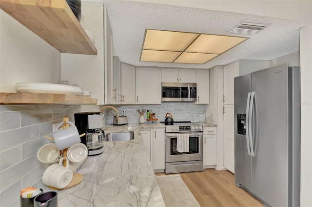 kitchen featuring light stone counters, sink, light hardwood / wood-style flooring, backsplash, and appliances with stainless steel finishes