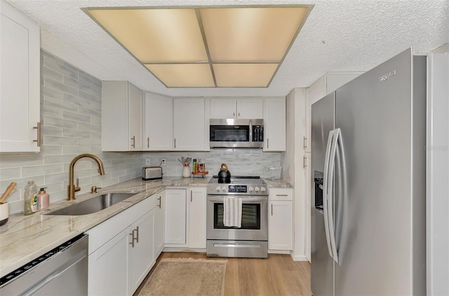 kitchen with light wood-type flooring, light stone counters, sink, white cabinetry, and appliances with stainless steel finishes