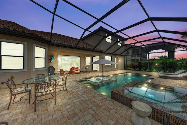 pool at dusk with an in ground hot tub, a lanai, and a patio area