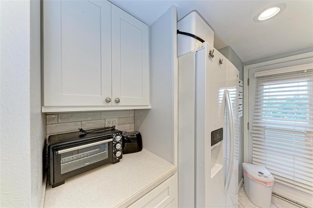 kitchen featuring white cabinets, white refrigerator with ice dispenser, and backsplash